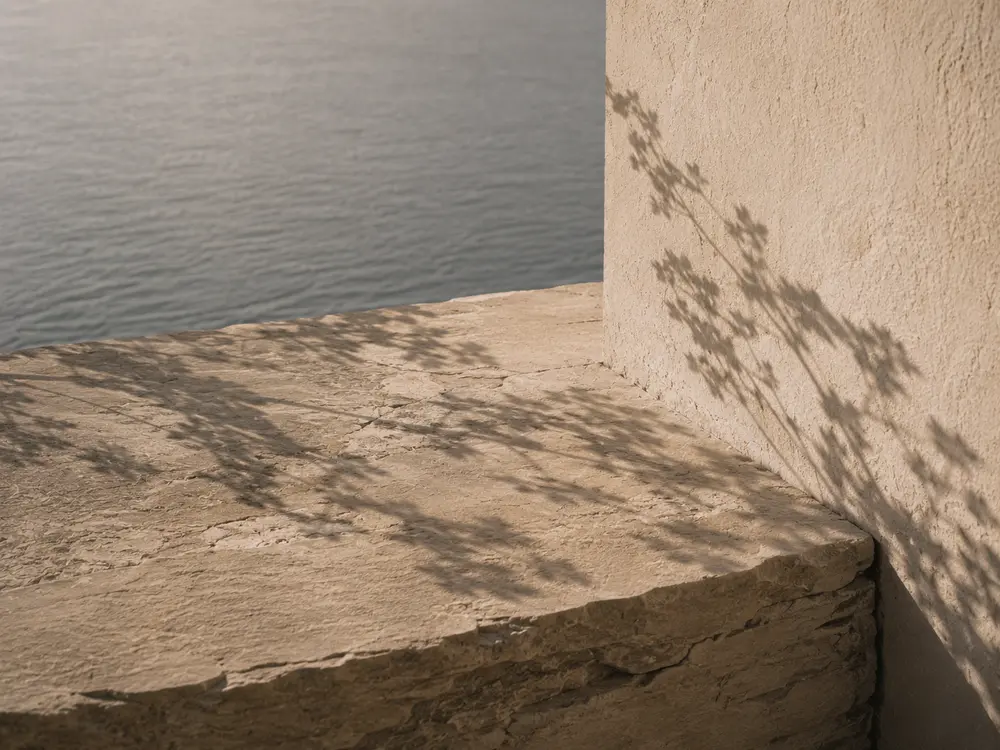 Tree shadow falling on a stone ledge and plaster corner above the sea