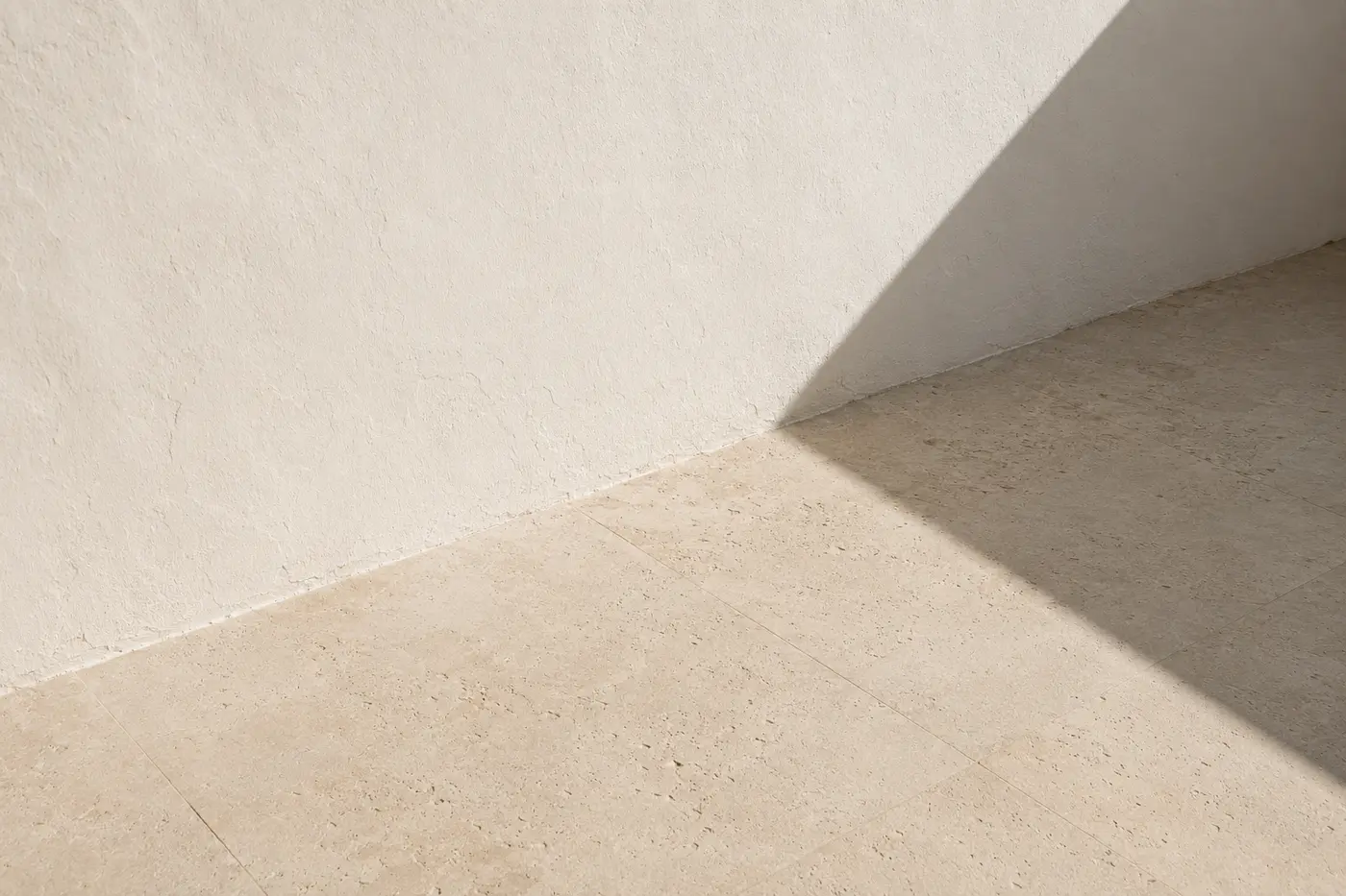 A white plaster wall meeting a pale limestone floor, crossed by a single crisp shadow