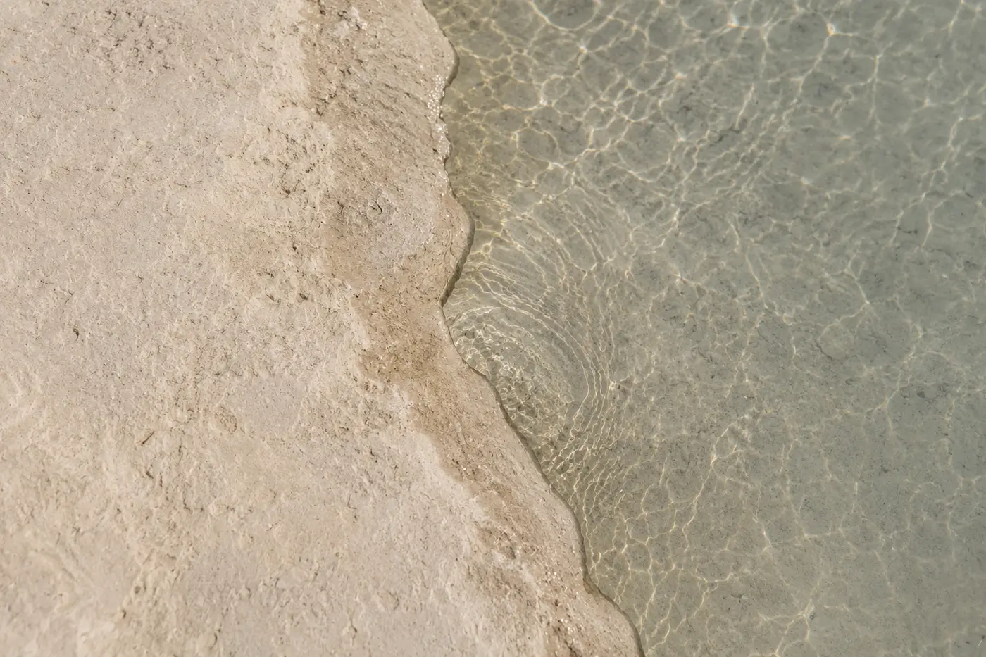 Seen from above, still clear water meeting worn pale limestone along a soft edge