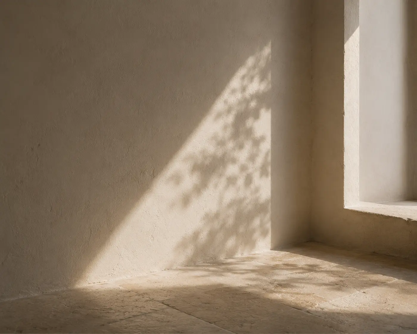 An almost empty room with a plaster wall, limestone floor and soft morning light from a window
