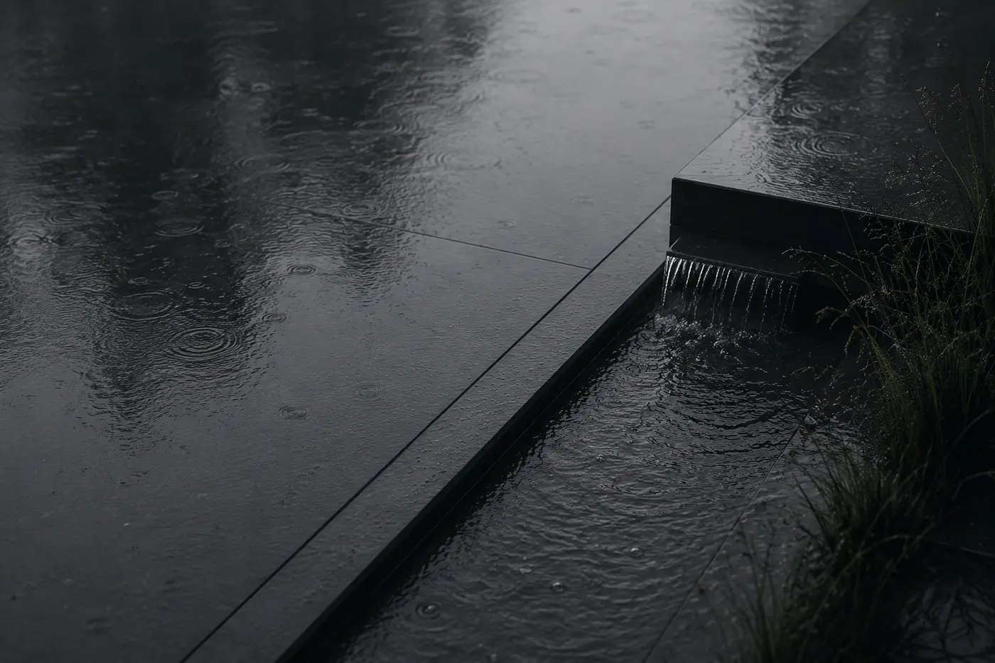 Rain falling on a dark stone water channel, water spilling over its edge